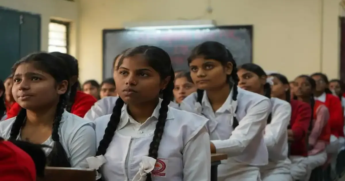 A student writing diligently during the Tamil Nadu Class 10 SSLC Mathematics board exam in a well-lit examination hall.