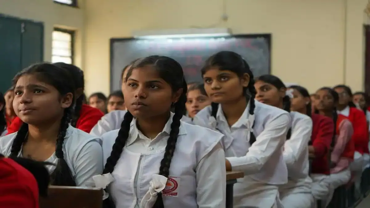 A student writing diligently during the Tamil Nadu Class 10 SSLC Mathematics board exam in a well-lit examination hall.