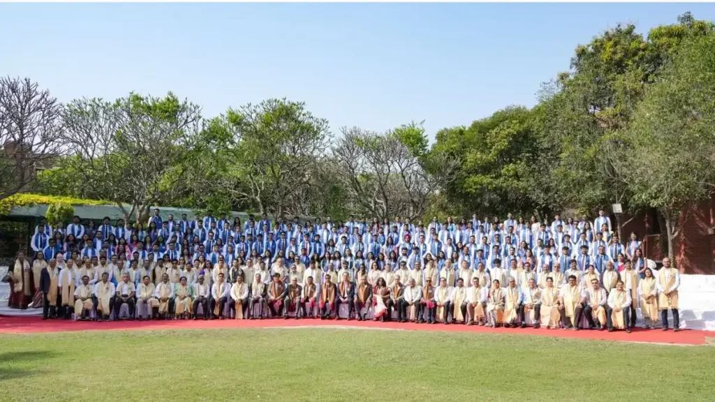 Graduating students in caps and gowns at a prestigious B-School convocation ceremony, listening to a speaker.