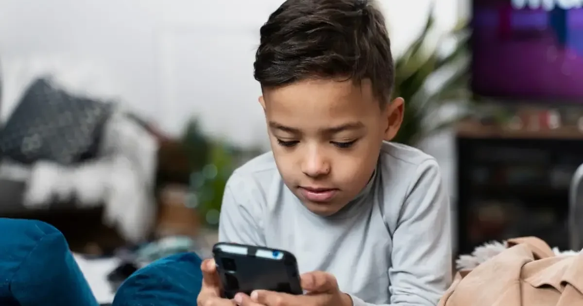 A high school student looking thoughtfully at their smartphone while sitting at a desk with books, illustrating the concept of student digital wellness.