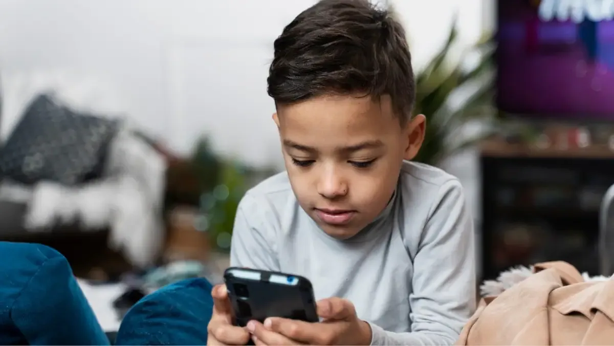 A high school student looking thoughtfully at their smartphone while sitting at a desk with books, illustrating the concept of student digital wellness.